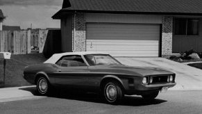 A 1973 Ford Mustang parks next to an attached garage.