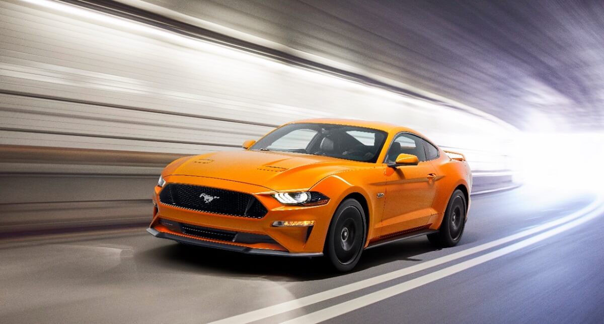 An orange 2018 Ford Mustang GT cruises through a tunnel.
