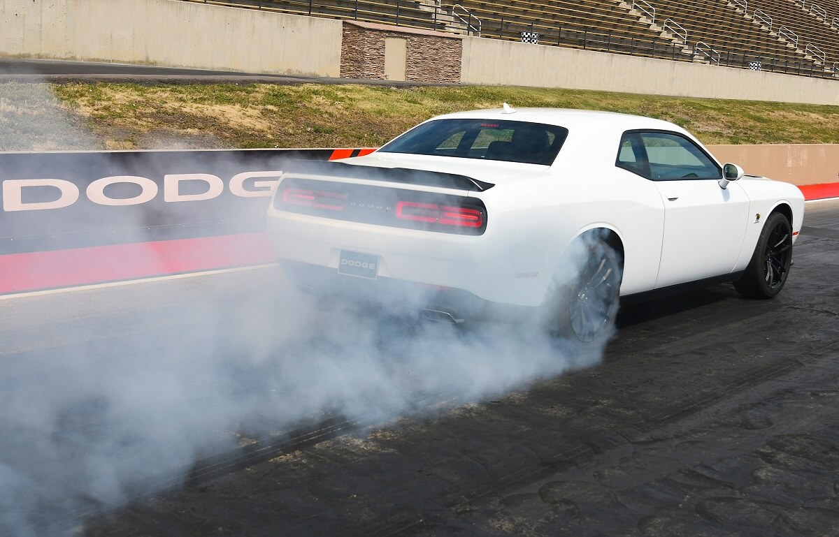 A white Dodge Challenger 1320 muscle car does a burnout.