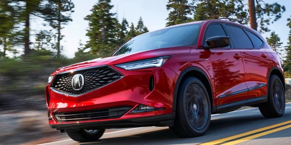 A red 2023 Acura MDX luxury midsize SUV is driving on the road. 