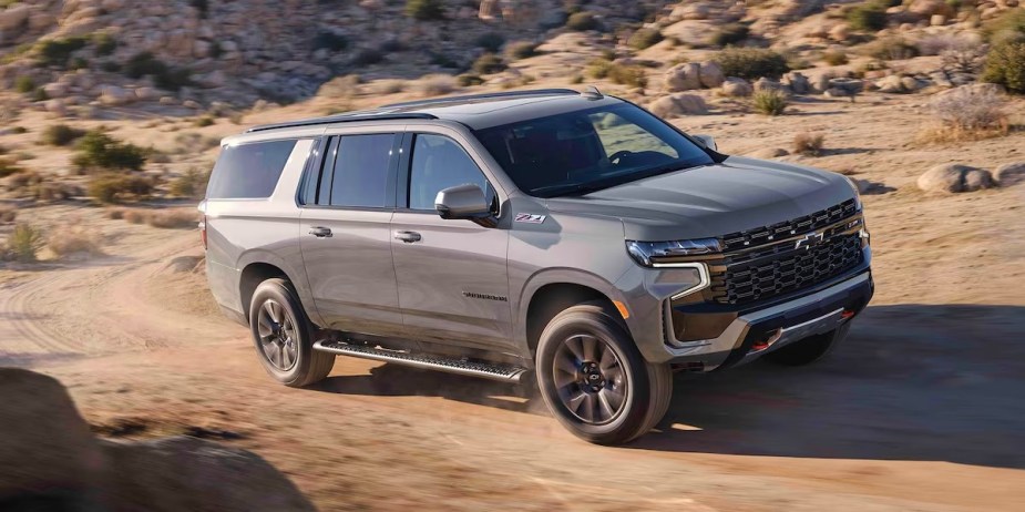 A gray 2023 Chevrolet Suburban full-size SUV is driving off-road. 