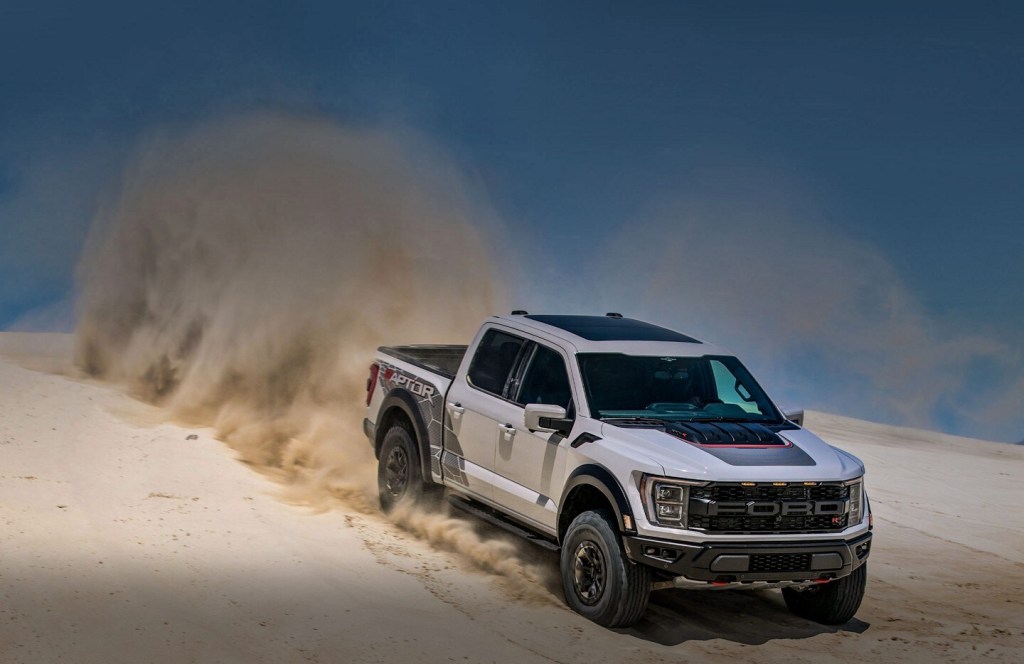The 2023 Ford F-150 Raptor driving down a hill in the sand is a powerful and expensive new pickup truck