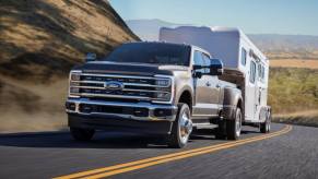 A 2023 Ford Super Duty F-350 Lariat heavy-duty pickup truck model towing a trailer up a country highway hill