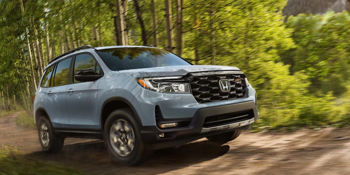 A blue 2023 Honda Passport midsize SUV is driving off-road. 