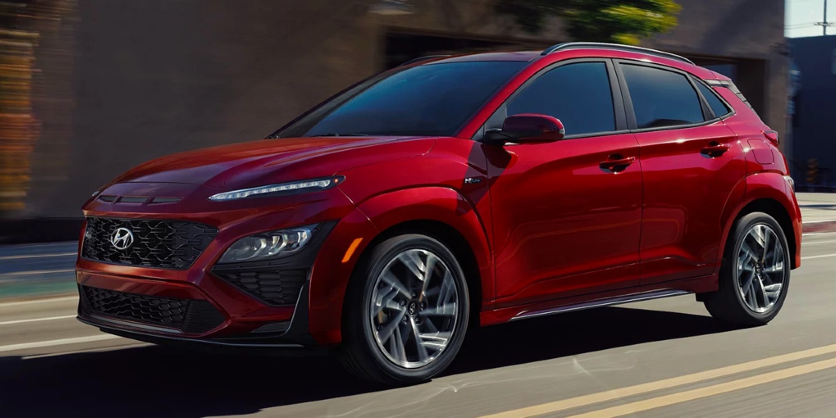A red 2023 Hyundai Kona subcompact SUV is driving on the road. 