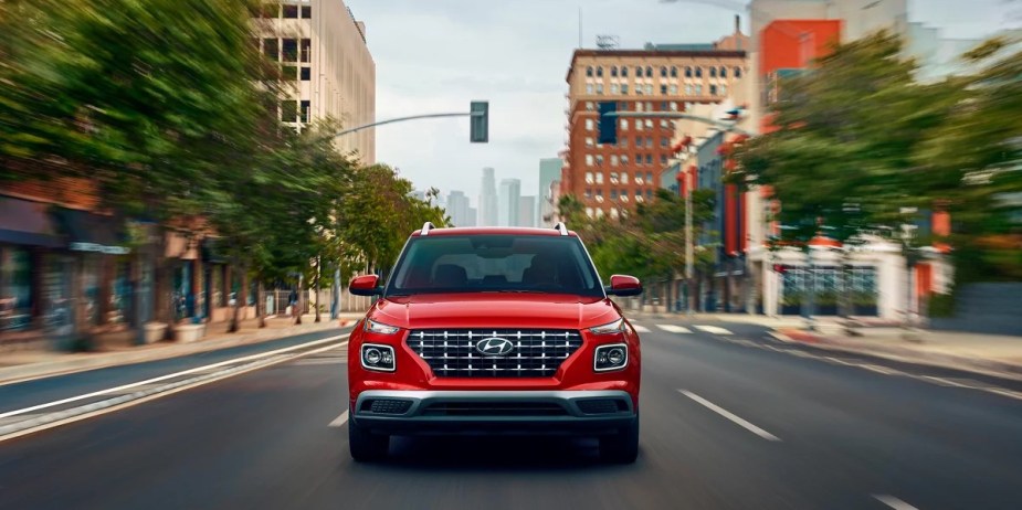 A red 2023 Hyundai Venue subcompact SUV is driving on the road. 