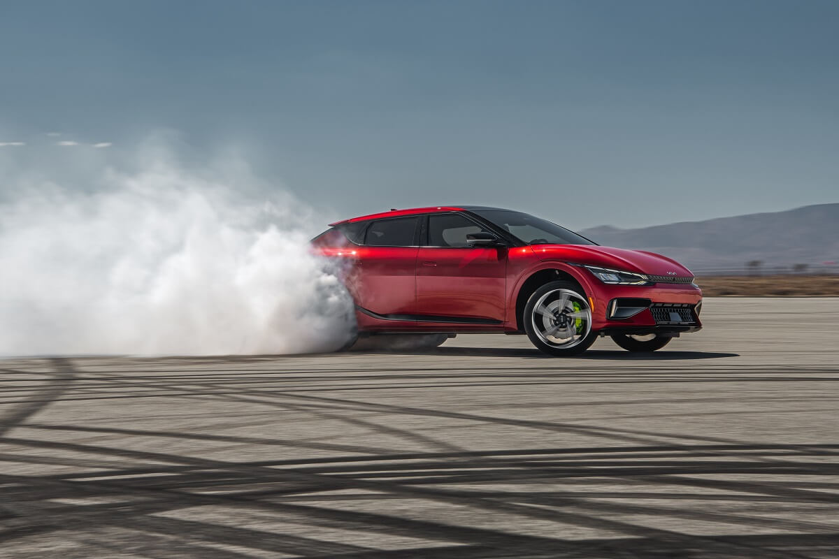A bright red 2023 Kia EV6 GT does a burnout on a skidpad.