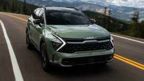A green 2023 Kia Sportage small SUV is driving on the road.