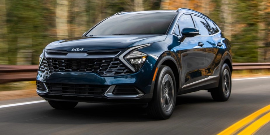 A blue 2023 Kia Sportage  small hybrid SUV is driving down the road. 