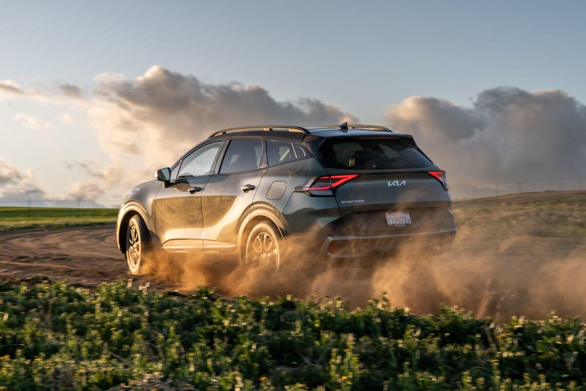 A 2023 Kia Sportage X-Pro compact SUV model driving on a dirt road kicking up dust clouds in the country