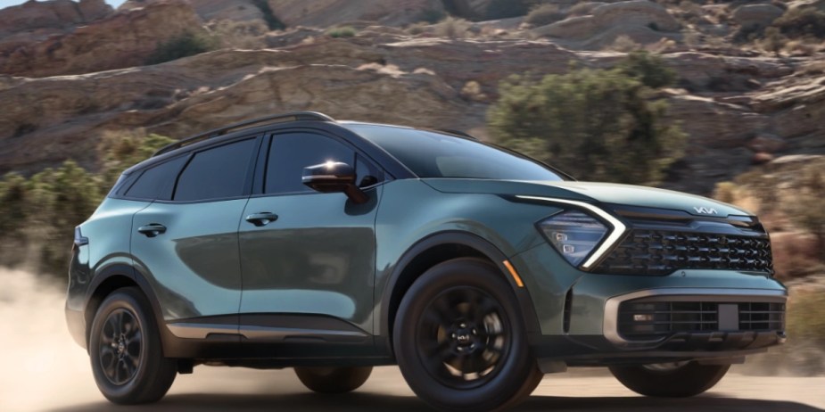 A green 2023 Kia Sportage Hybrid small SUV is driving off-road. 
