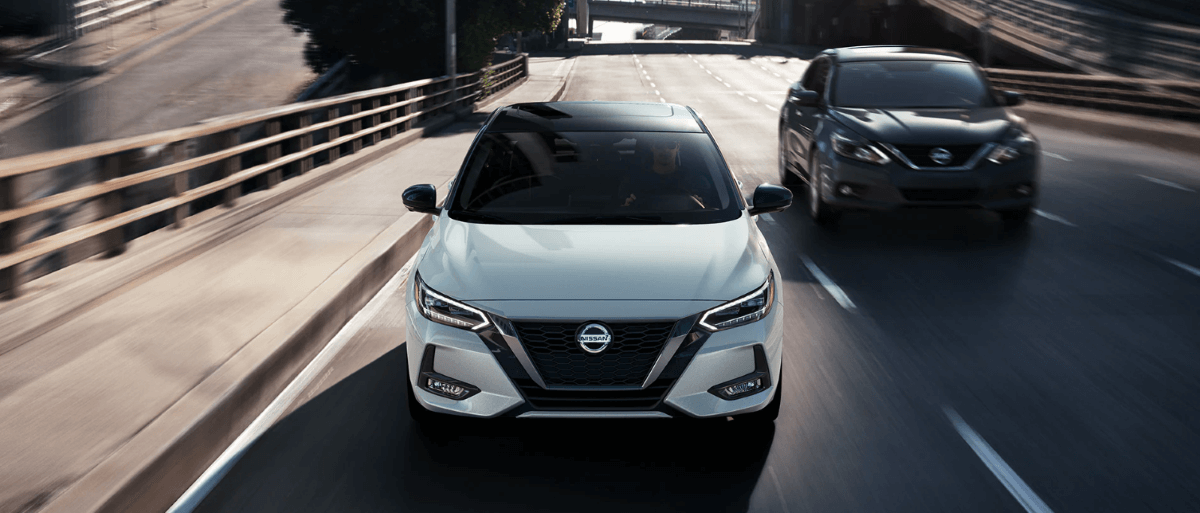 2023 Nissan Sentra compact sedan models in white and gray driving under a highway overpass bridge