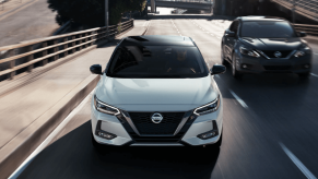 2023 Nissan Sentra compact sedan models in white and gray driving under a highway overpass bridge