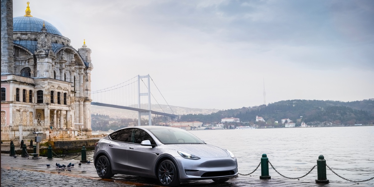A gray 2023 Tesla Model Y small electric SUV is parked by the water.