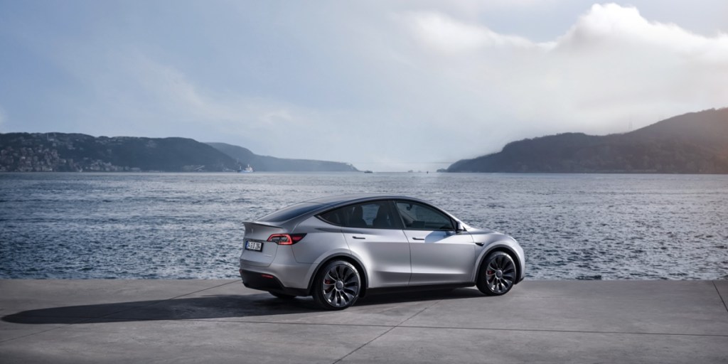 A gray 2023 Tesla Model Y small electric SUV is parked near water, it's part of yet another Tesla recall.