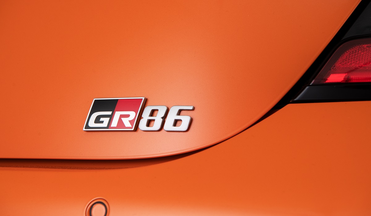 An orange 2023 Toyota GR86 flashes its rear badge.