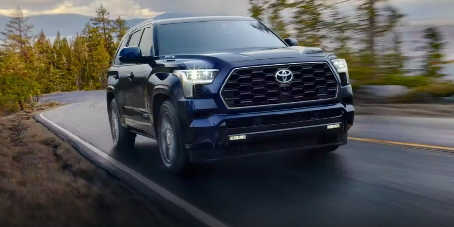 A blue 2023 Toyota Sequoia full-size SUV is driving on the road. 