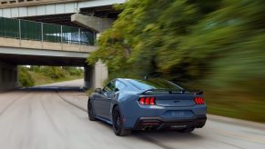 A blue 2024 Ford Mustang GT drives down a park road.