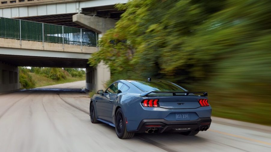 A blue 2024 Ford Mustang GT drives down a park road.