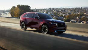 The new 2024 Mazda CX-90 – pictured here in burgundy driving on the road – is one of the new additions to Mazda sales figures.