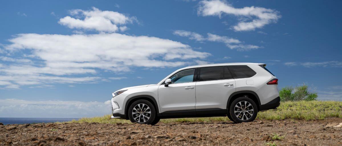 A side profile shot of a 2024 Toyota Grand Highlander Limited midsize SUV model parked on a cliff overlooking the sea