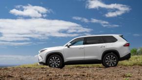 A side profile shot of a 2024 Toyota Grand Highlander Limited midsize SUV model parked on a cliff overlooking the sea
