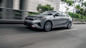 One of the most affordable Kia sedans is the Kia Forte, pictured in silver/gray speeding down a city road.