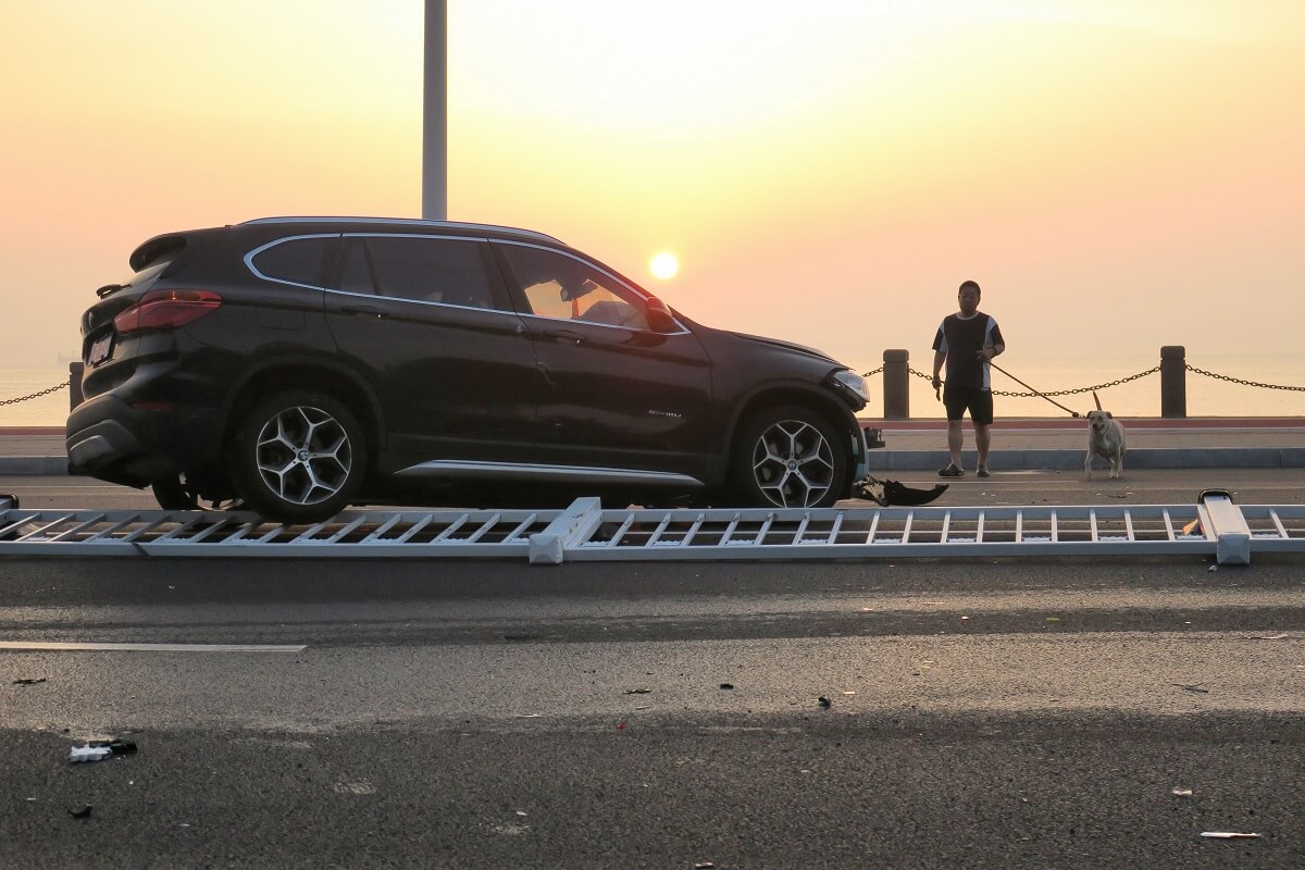 A BMW X3 luxury SUV sits on a safety barrier after a crash.