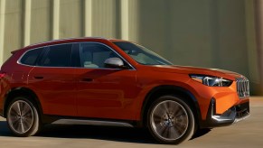 An orange 2023 BMW X1 luxury subcompact SUV is driving on the road.