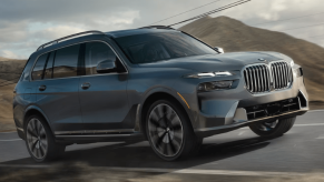 A 2024 BMW X7 full-size luxury SUV model driving down a country highway past phone lines