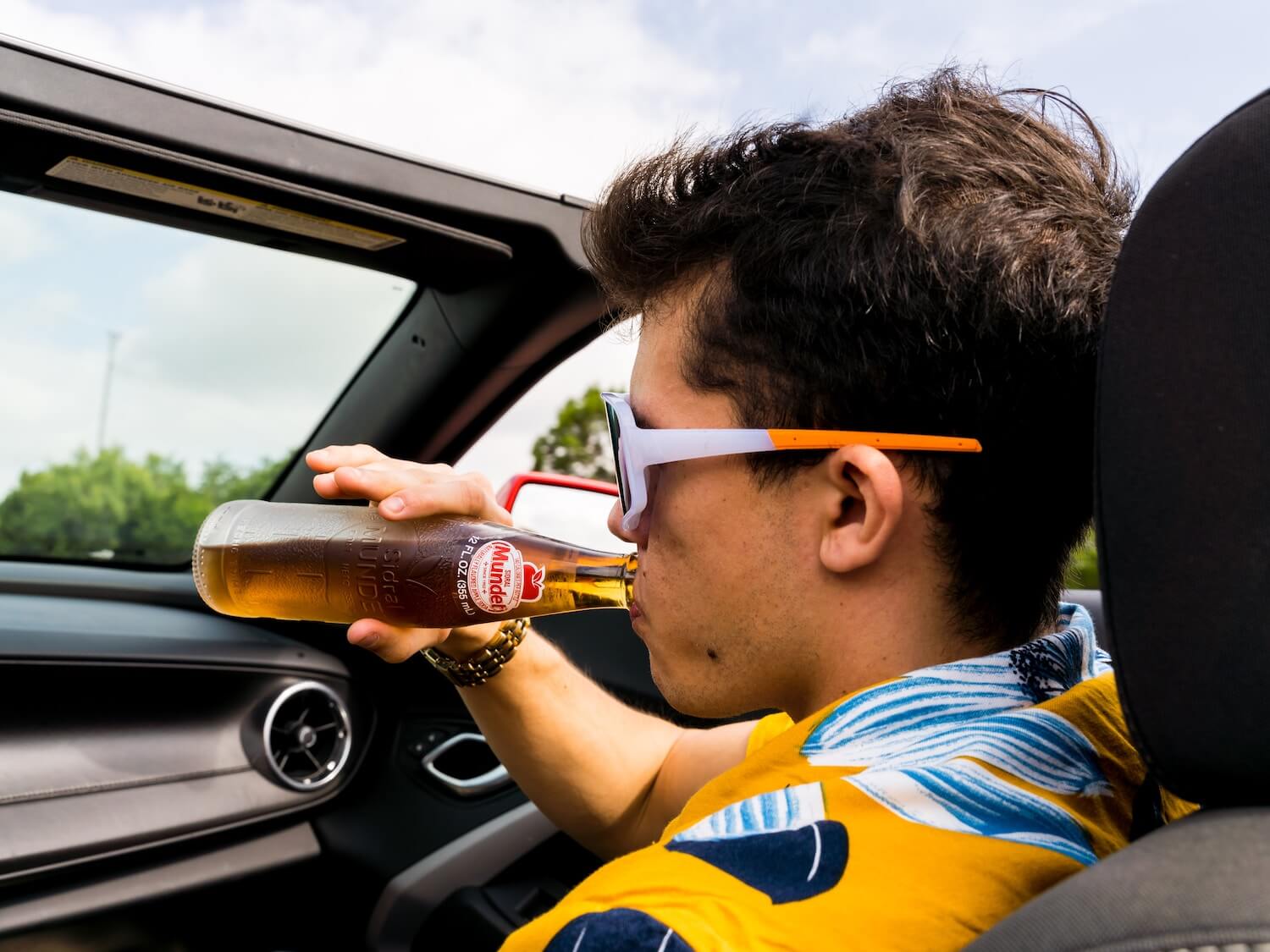 A young man drinking a beer in a car while it drives along. 