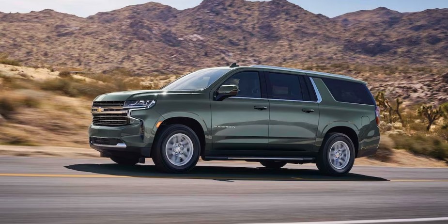 A green 2023 Chevrolet Suburban full-size SUV is driving on the road. 