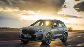 A BMW X1 M35i xDrive subcompact SUV model in Frozen Pure Grey Metallic with a sunset behind it