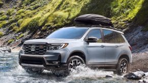A gray 2023 Honda Passport midsize SUV is driving through shallow water off-road.