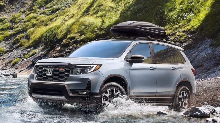 A gray 2023 Honda Passport midsize SUV is driving through shallow water off-road.
