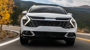 A white 2023 Kia Sportage small SUV is driving on the road.