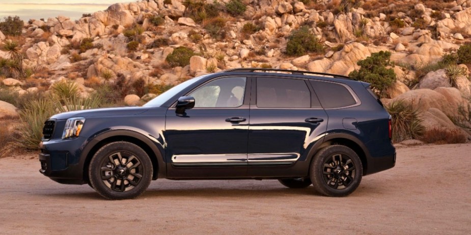 A blue 2024 Kia Telluride midsize three-row SUV parked in dirt, its warranty is among the best.