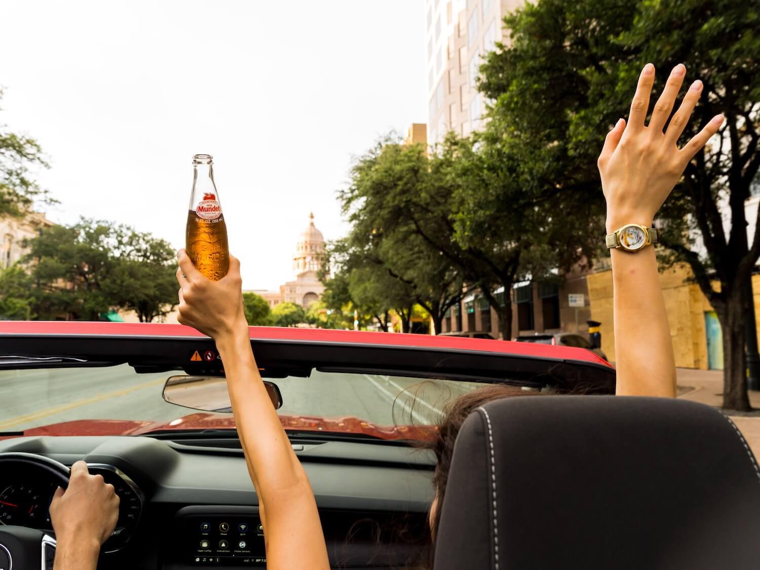 A convertible passenger holding an open container of alcohol above their head.