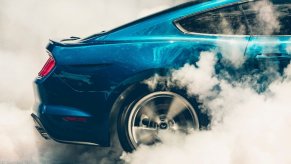 A bright blue S550 Ford Mustang roasts its tires in typical muscle car fashion.