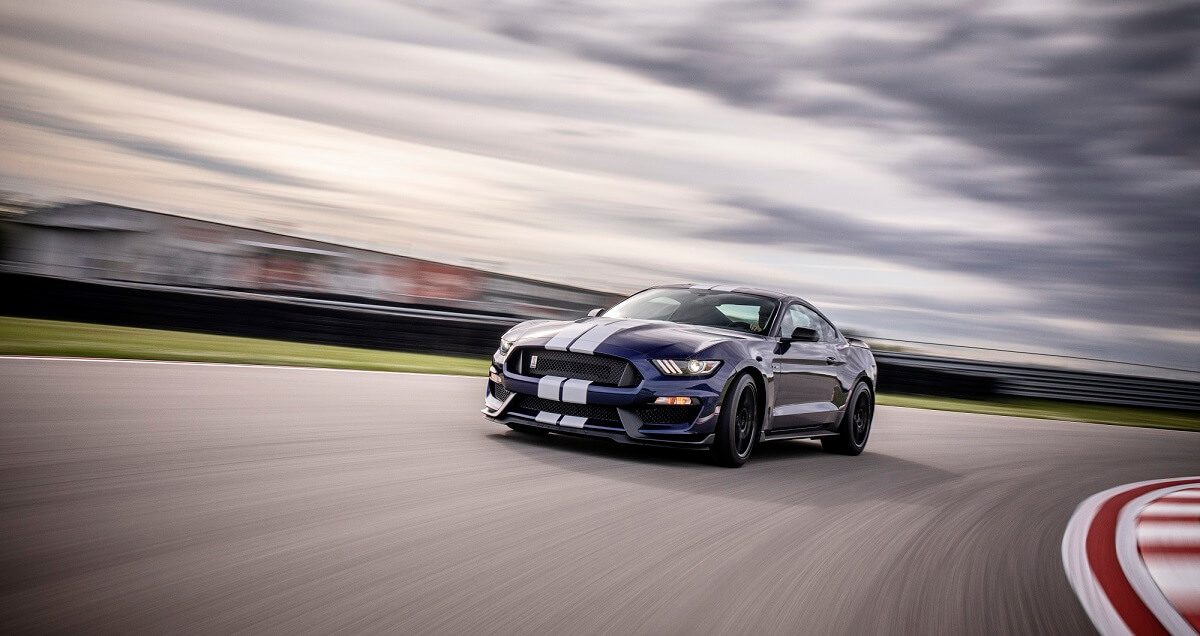 A blue and white S550 Ford Mustang Shelby GT350 corners on a track.
