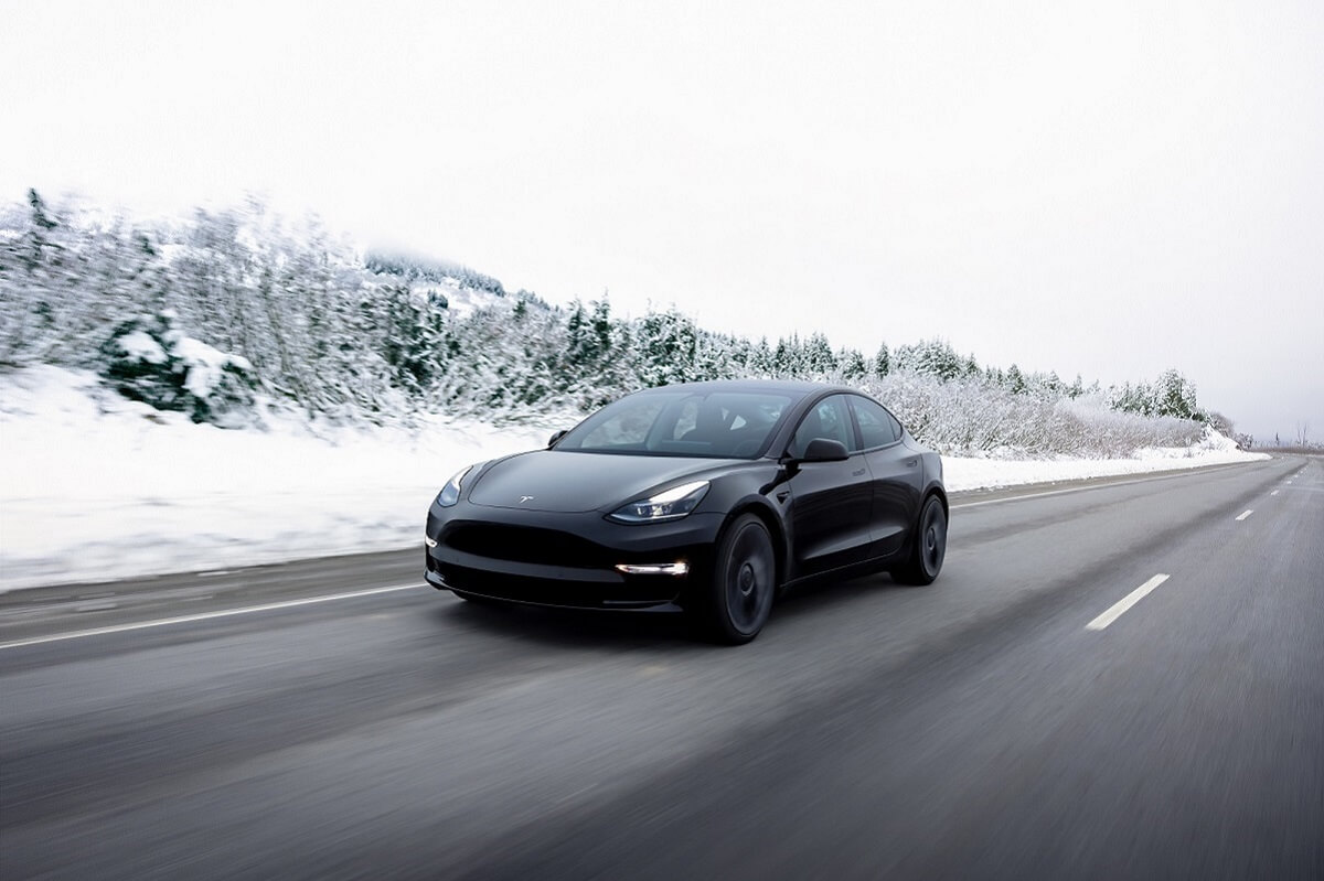 A black 2023 Tesla Model 3 drives past a snowy landscape.