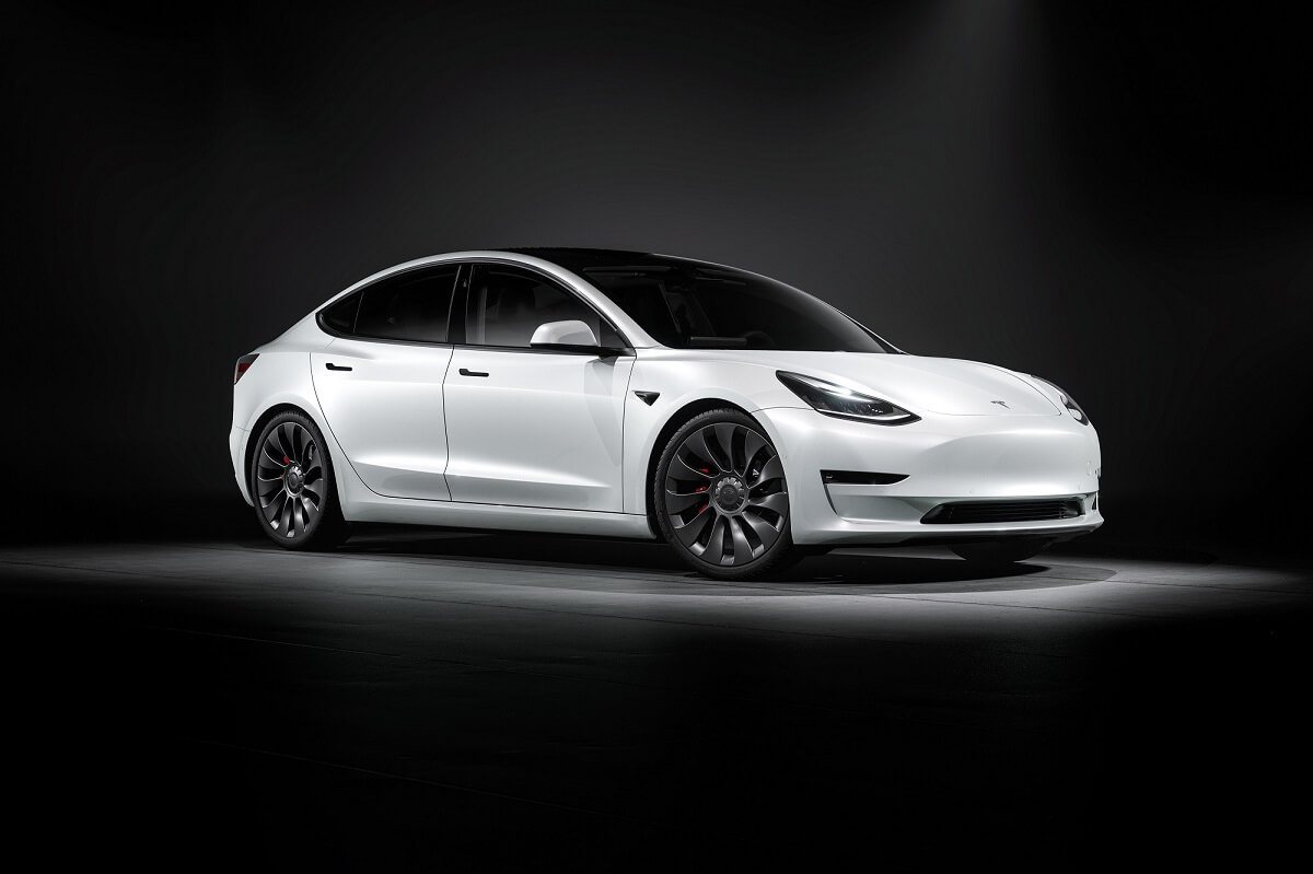 A white 2023 Tesla Model 3 parks under overhead lighting on a stage