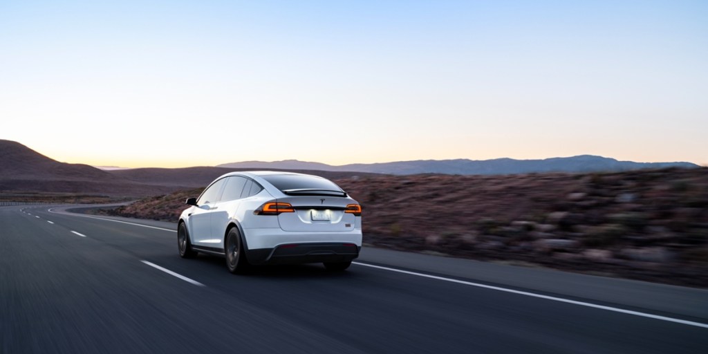 A white 2023 Tesla Model X is driving down the road.