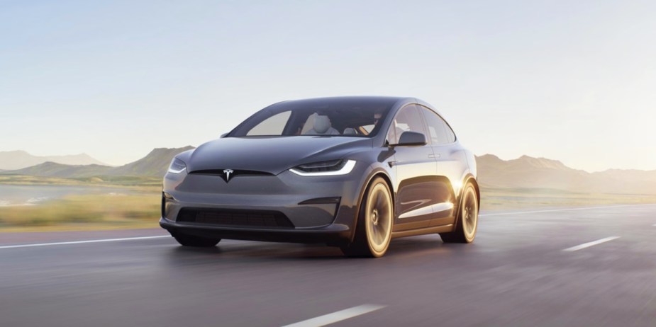A gray 2023 Tesla Model X electric midsize SUV is driving on the road. 