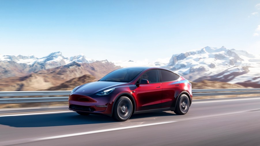 A red 2023 Tesla Model Y small electric SUV is driving on the road.