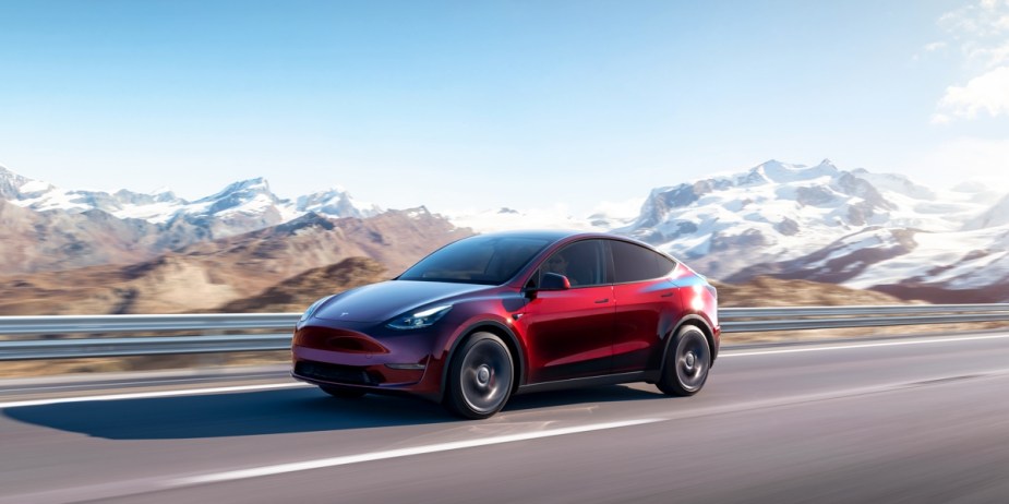 A red 2023 Tesla Model Y small electric SUV is driving on the road. 