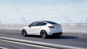 A white 2023 Tesla Model Y small electric SUV is driving on a bridge.