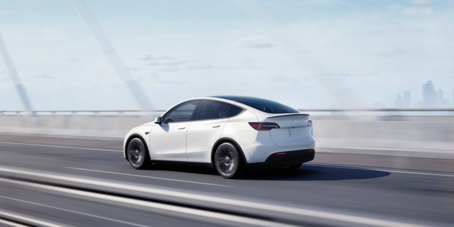 A white 2023 Tesla Model Y small electric SUV is driving on a bridge. 
