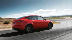 A red 2023 Tesla Model Y small electric SUV is driving on the road.