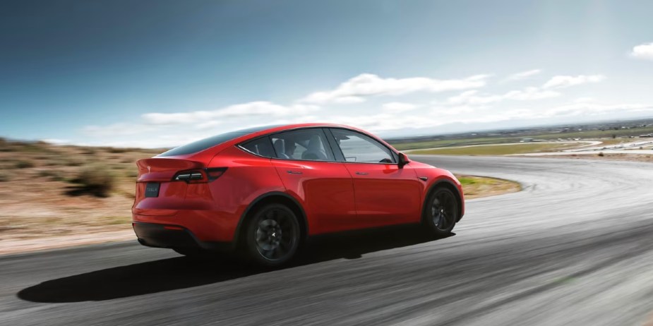 A red 2023 Tesla Model Y small electric SUV is driving on the road. 